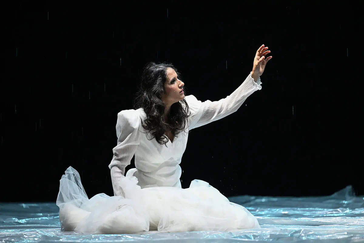 Escena de Hamlet con una intérprete vestida de blanco arrodillada sobre el escenario.