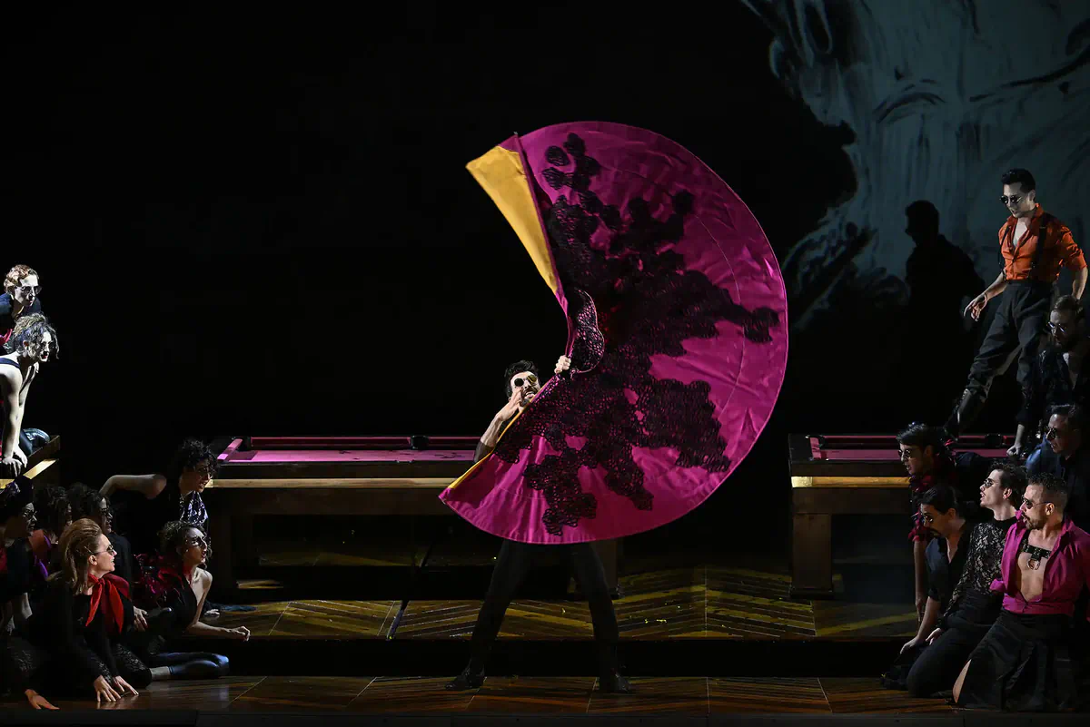 Escena de La traviata con un intérprete sosteniendo un gran abanico de color fucsia sobre el escenario.