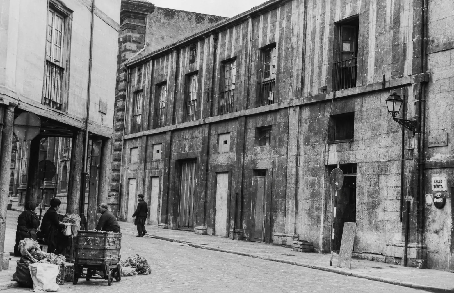 Vista histórica del antiguo Corral de Comedias de Oviedo, con fachada de piedra en una calle estrecha y varias personas en primer plano