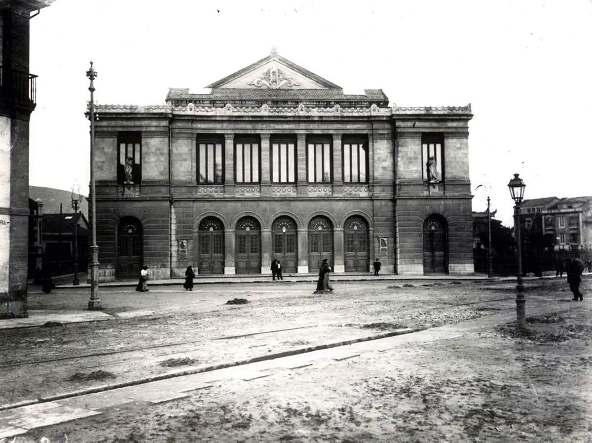 Vista de la fachada del Teatro Campoamor en el año 1892, de estilo neoclásico y varias personas en la plaza situada frente al teatro.